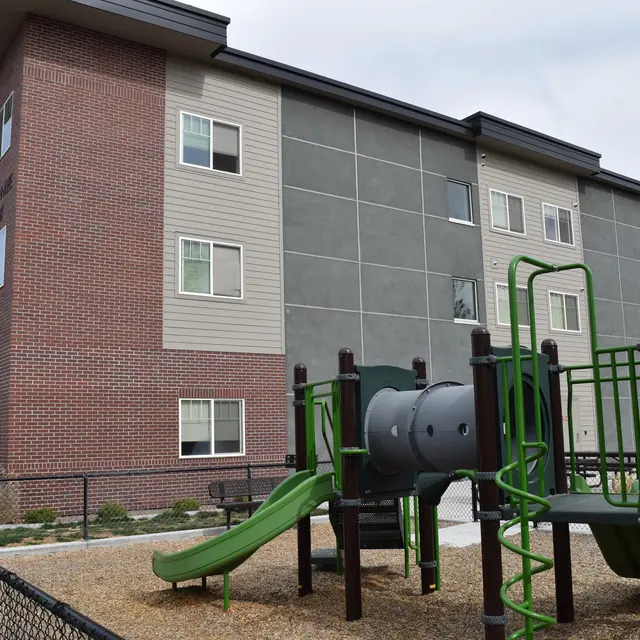 Apartment Building with Playground An apartment building with a playground in front, featuring slides and climbing structures.