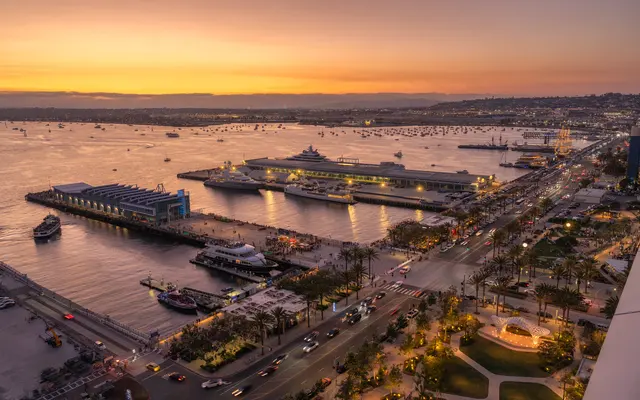 Aerial view of a harbor at sunset with boats docked and a bustling waterfront area.