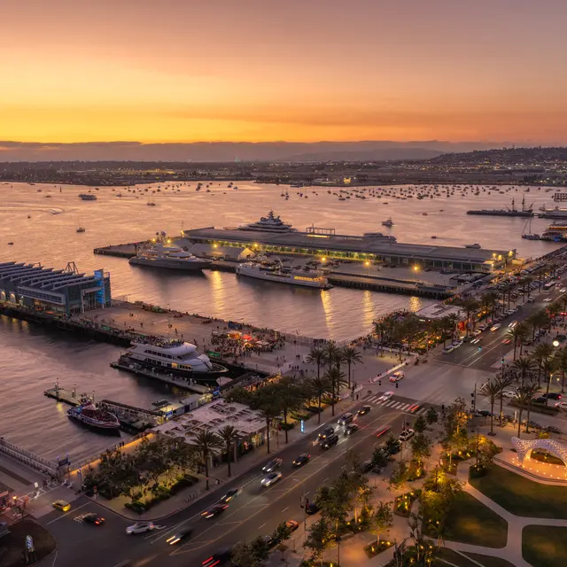 Aerial view of a harbor at sunset with boats docked and a bustling waterfront area.