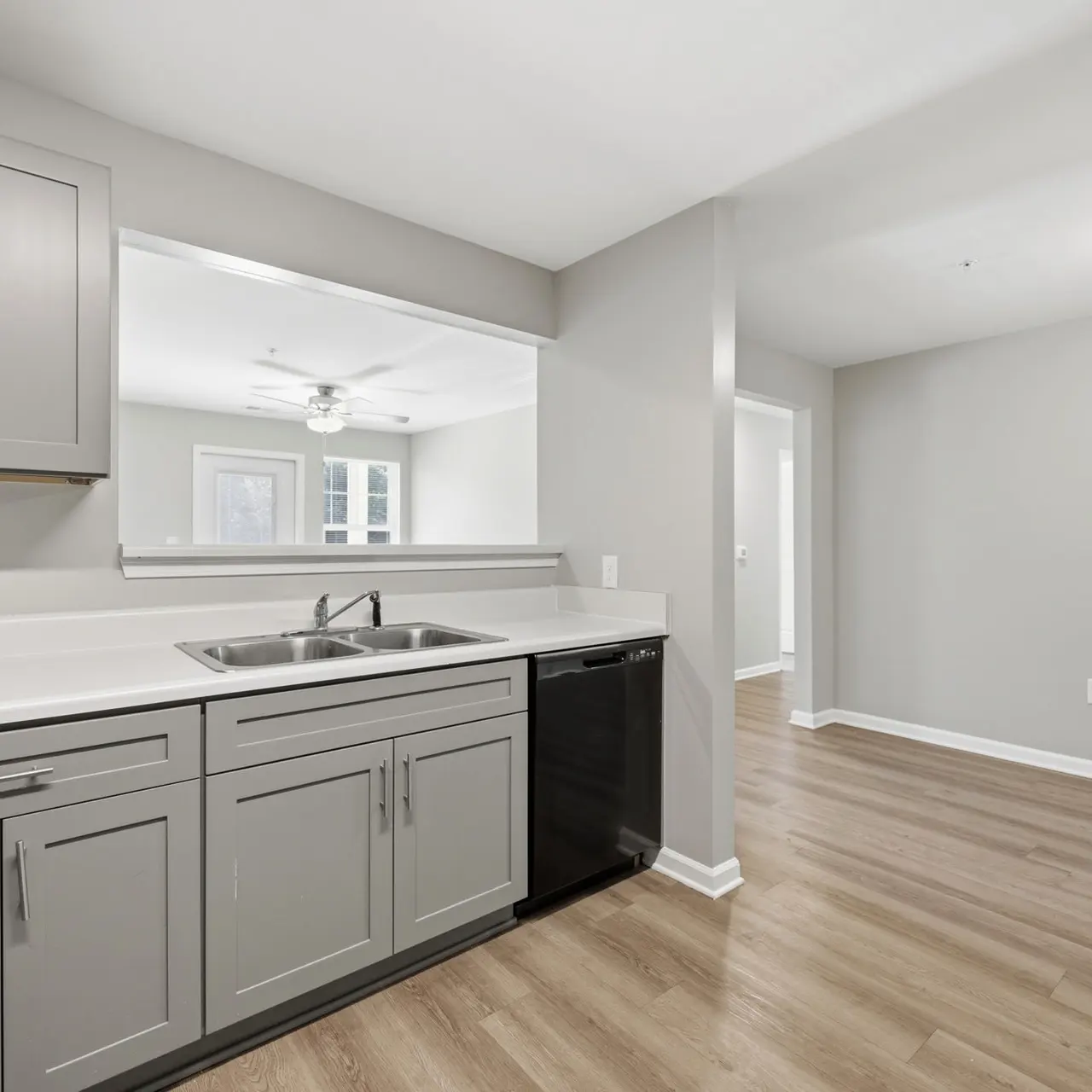 A modern kitchen with gray cabinets, a double sink, and a dishwasher, featuring light-colored flooring and neutral walls.