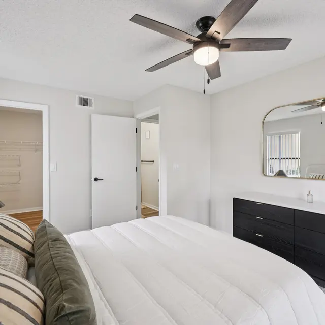 A cozy modern bedroom featuring a queen-sized bed, black dresser, and ceiling fan.