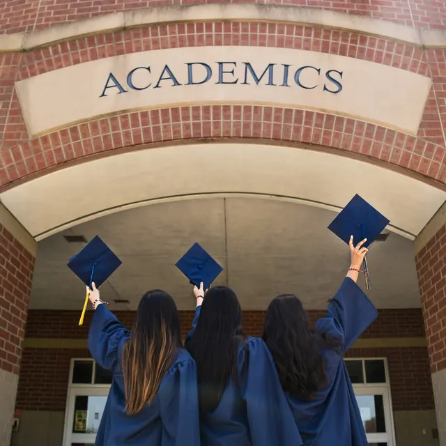 Texas Southern University Four graduates in blue gowns holding caps in the air in front of a building with the word 'ACADEMICS' above them.