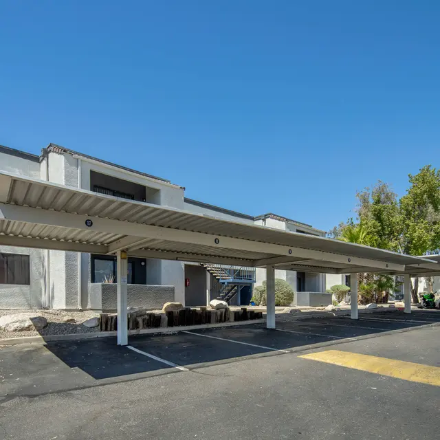 A parking area with covered spaces beside a two-story white building under a clear blue sky.