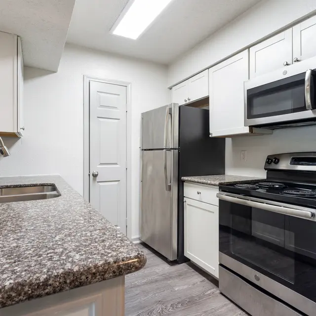 A modern kitchen featuring granite countertops, stainless steel appliances, and white cabinetry. Includes a sink and an oven with a stove.