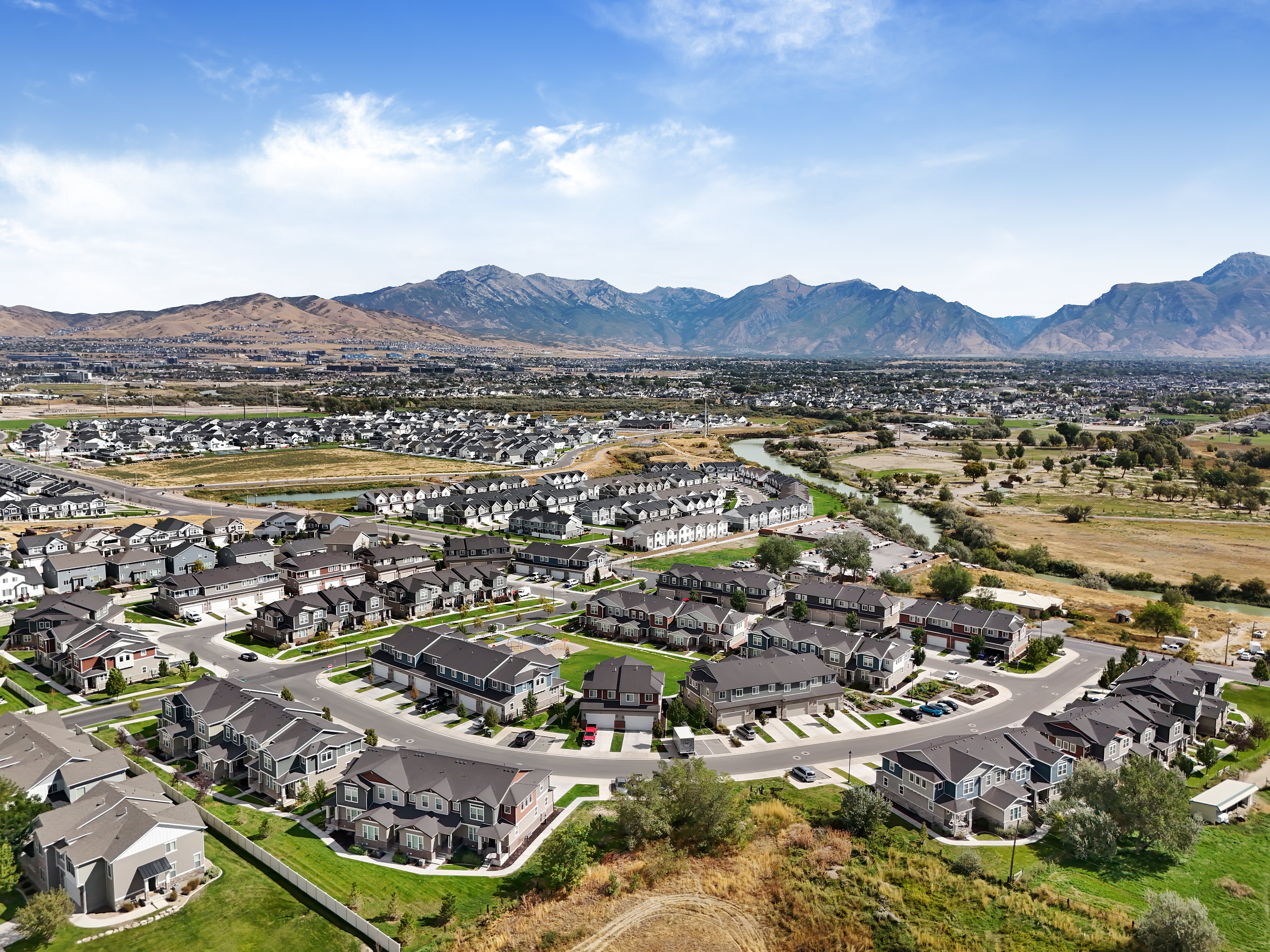 Aerial view of a suburban neighborhood with modern houses arranged in circular patterns, surrounded by greenery and mountains in the background.