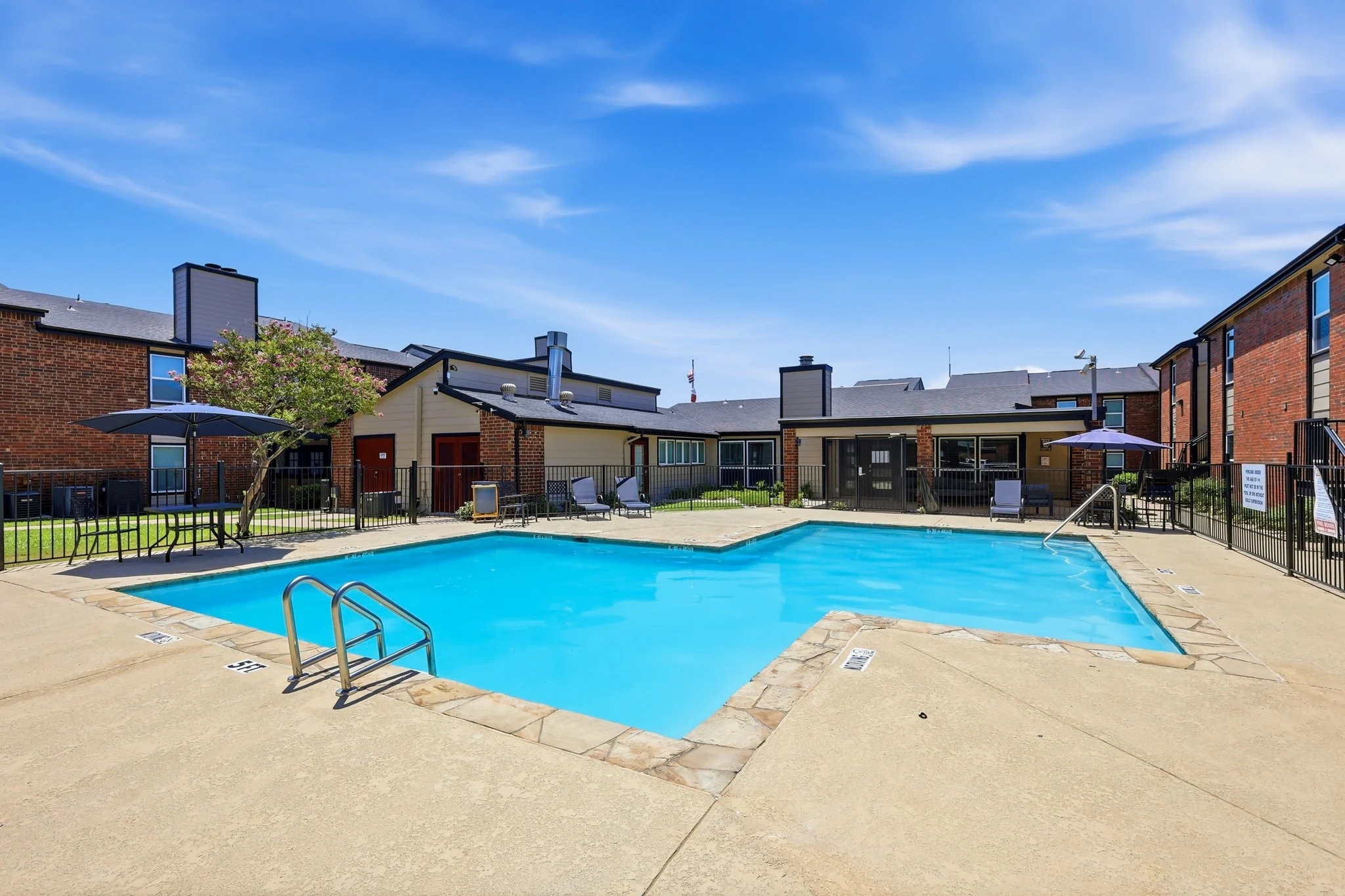 Inviting Community Pool A clear swimming pool surrounded by a fenced area with lounge chairs and umbrellas, adjacent to residential buildings.
