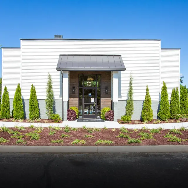 Contemporary Building Entrance A modern building with a landscaped front, featuring tall green plants and a decorative entrance.