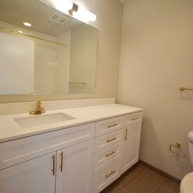 Modern Bathroom Design A modern bathroom featuring a white vanity with gold hardware, a large mirror, and tiled flooring.