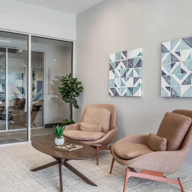 Modern Office Lobby Design A modern office lobby featuring two stylish chairs, a coffee table, a small plant, and framed geometric artwork on the wall.