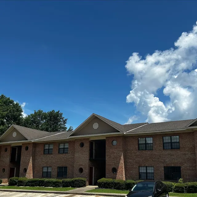Apartment Building on a Sunny Day A brick apartment building under a bright blue sky with fluffy white clouds.