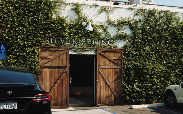 Exterior view of a building named Silver Springs, featuring wooden double doors framed by greenery and two parked cars in front.
