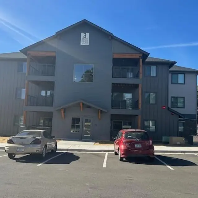 Modern Apartment Building Exterior view of a three-story gray apartment building with balconies and parked cars in front.