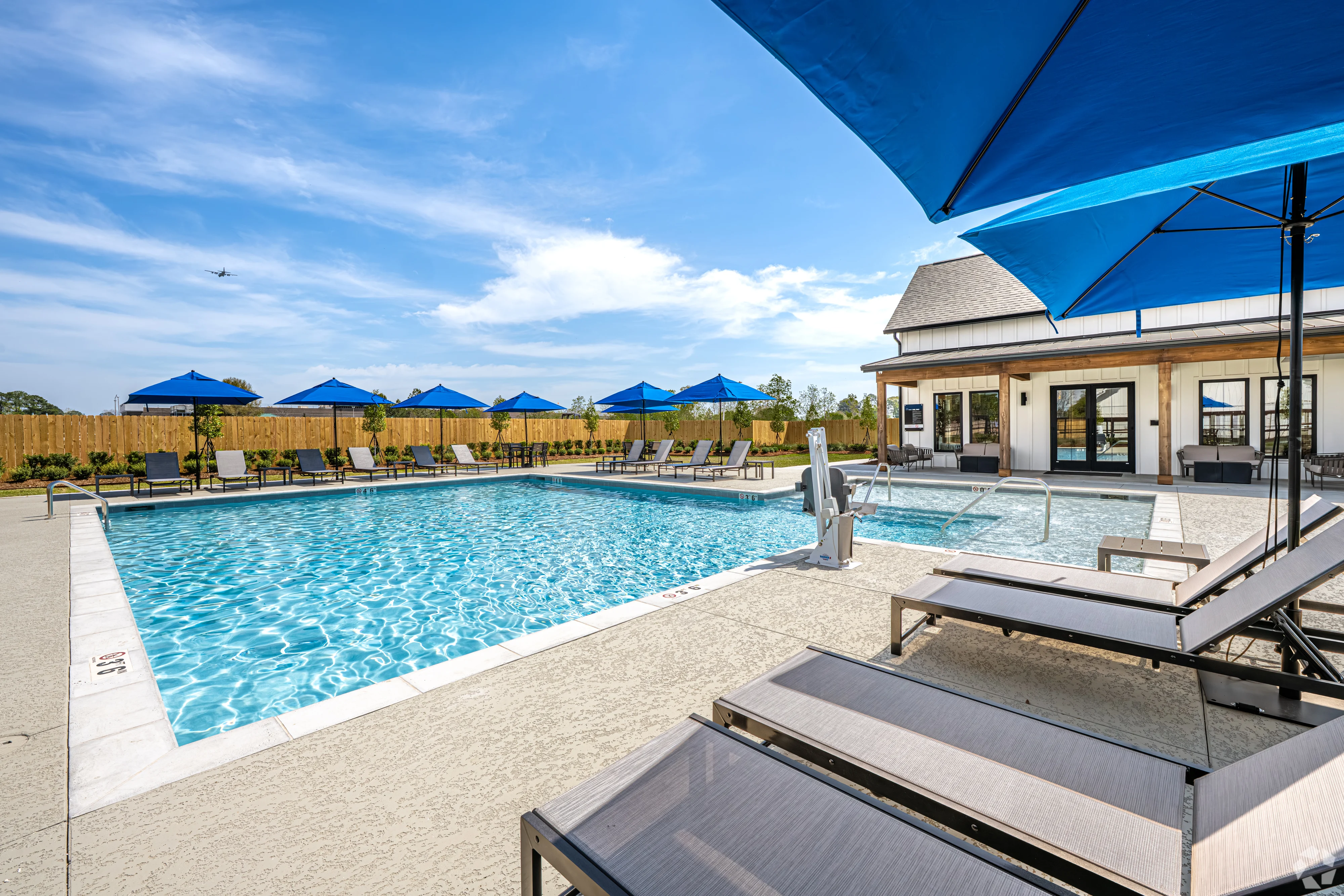 A spacious outdoor swimming pool area with lounge chairs and umbrellas, surrounded by greenery.