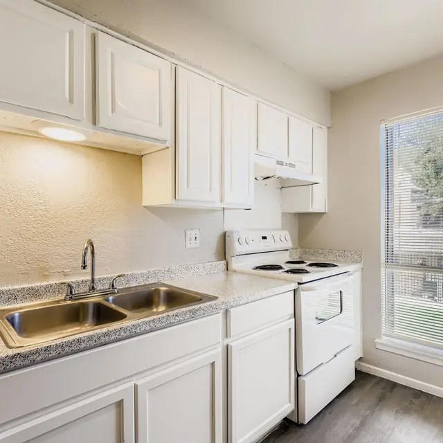 A bright kitchen featuring white cabinets, a stove, and a double sink with a window overlooking an outdoor view.