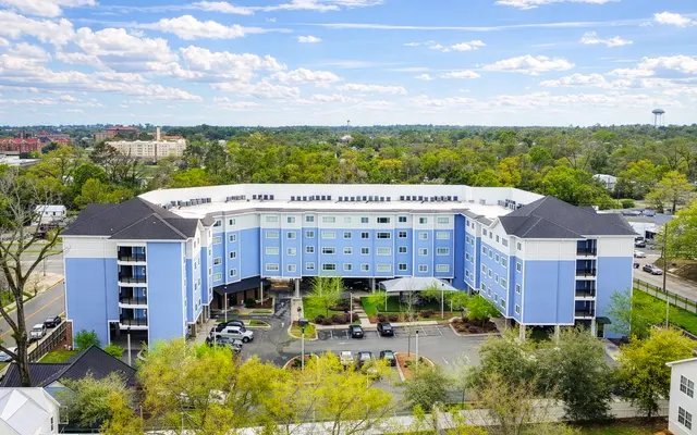 Aerial view of a modern blue-colored apartment building with multiple levels surrounded by trees and parking spaces.