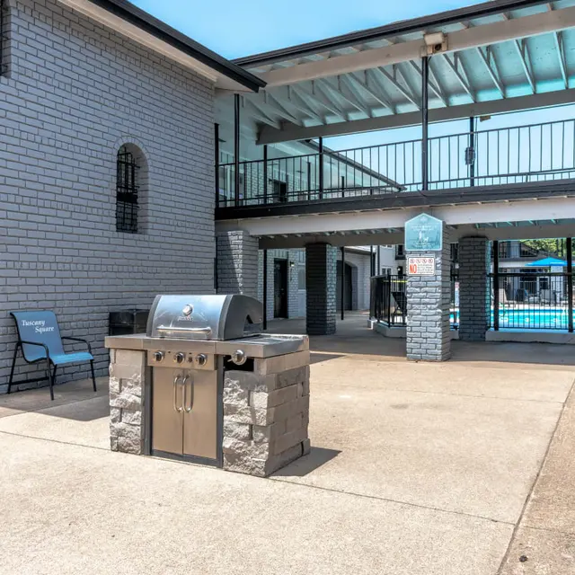 Grilling area with a barbecue grill and pool in the background at an apartment complex.