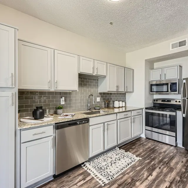 A contemporary kitchen featuring gray cabinets, stainless steel appliances, and a stylish backsplash with wooden flooring.