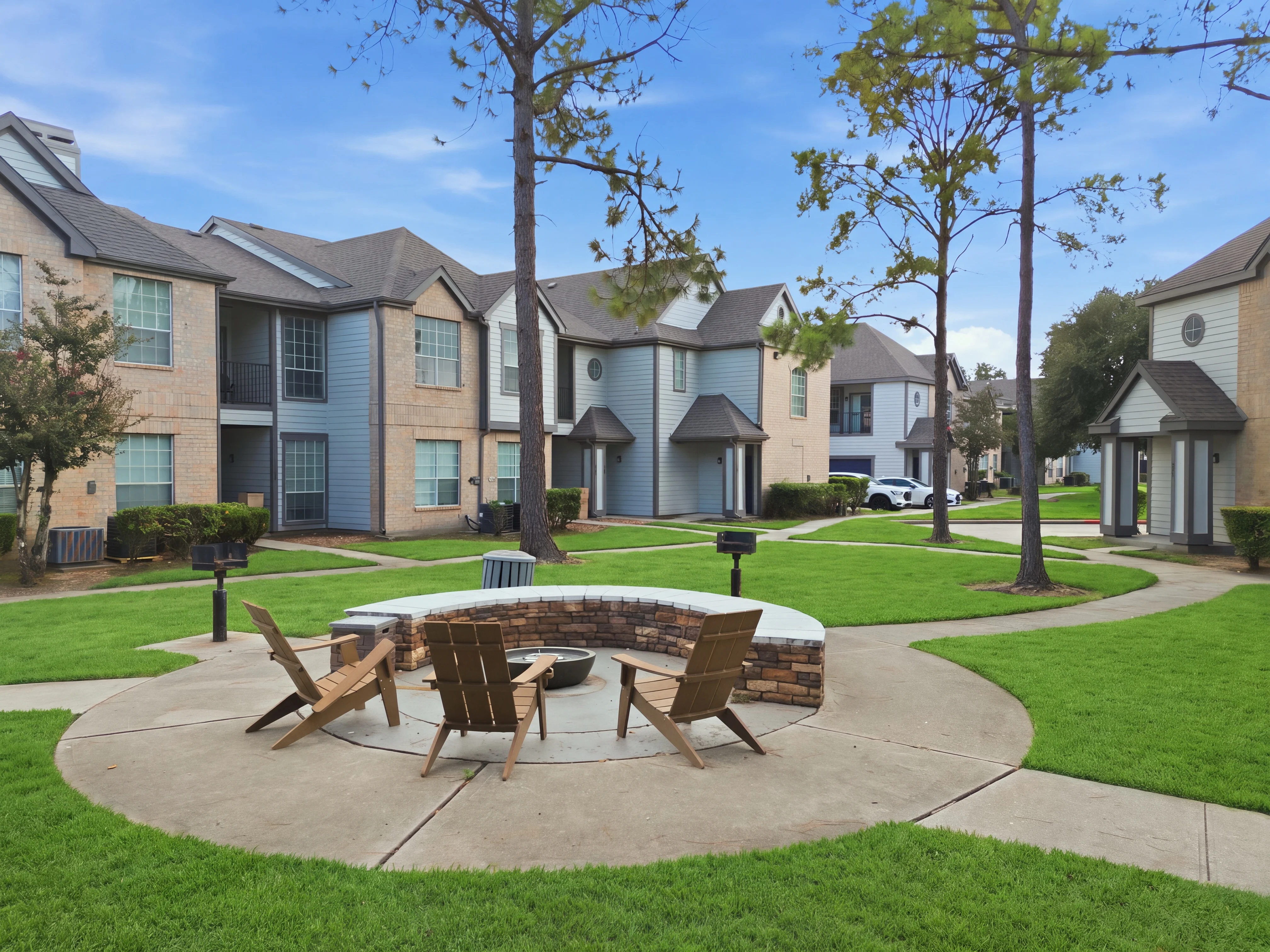 Welcoming Community Fire Pit Area A view of a landscaped community area featuring a fire pit surrounded by wooden chairs, with apartment buildings in the background.
