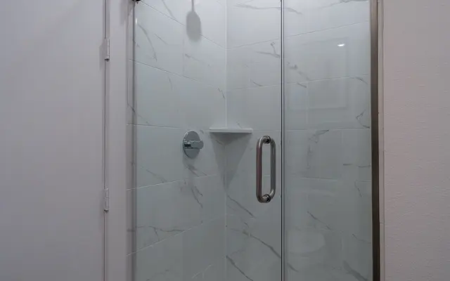 A modern shower with glass partition, white marble walls, and a wooden floor.