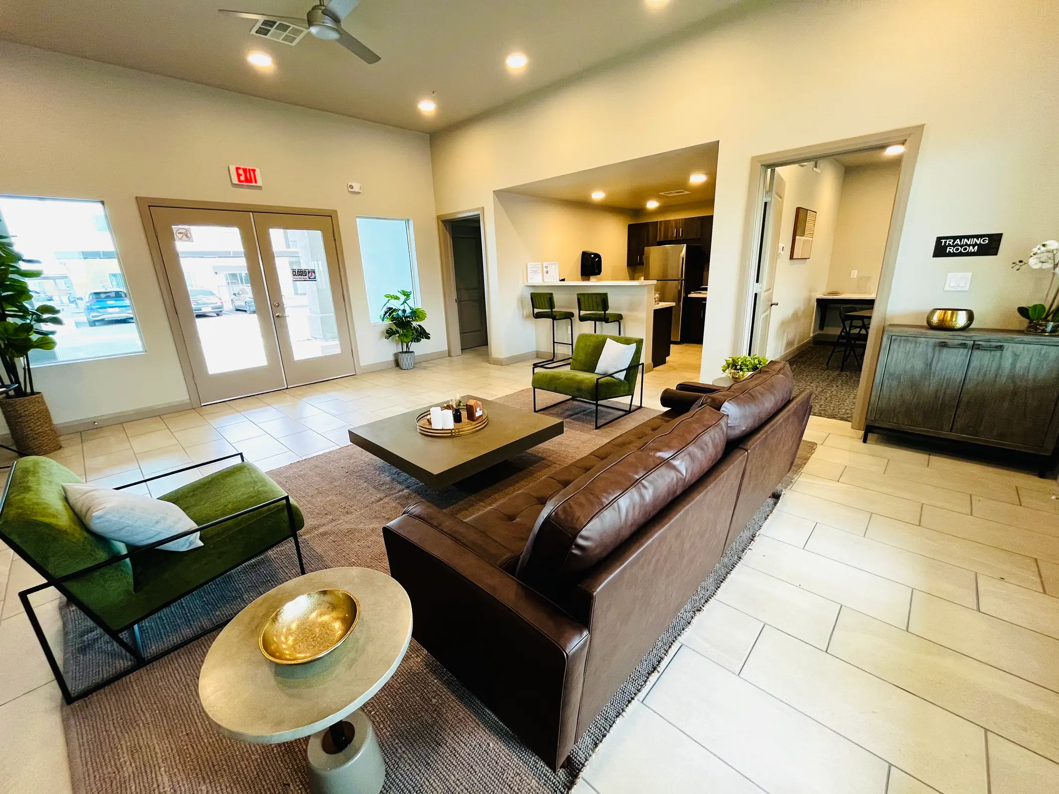 Community lounge with a sofa, green chairs and a kitchen counter.