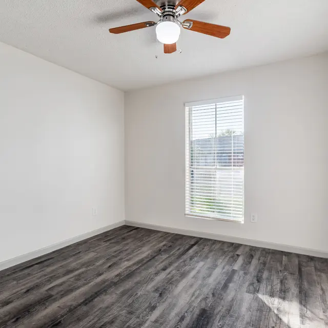 An empty room with hardwood floors and a ceiling fan.