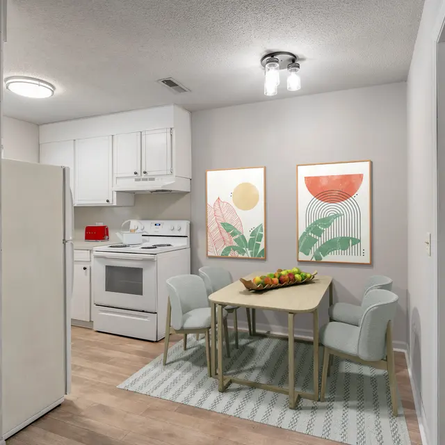 A modern kitchen and dining area featuring a white refrigerator, stove, and oven. A light-colored table with four chairs is set in the center, adorned with a bowl of fruit. Two large decorative framed prints featuring geometric designs hang on the wall. There is a soft area rug under the table.
