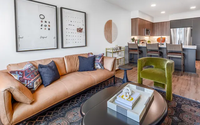 Modern Living Room Design A modern living room featuring a leather sofa, colorful throw pillows, coffee table, and a decorative rug with a kitchen in the background.