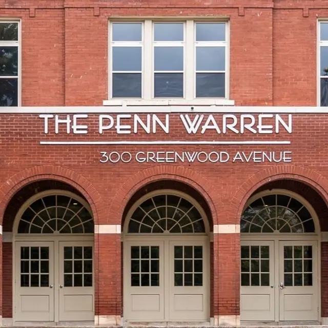 Exterior view of The Penn Warren building with red brick facade and three large arched doorways.