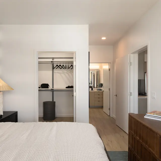 A modern bedroom featuring a geometric patterned accent wall, a cozy bed with decorative pillows, a stylish lamp, and a spacious closet. Two doorways lead to additional rooms.