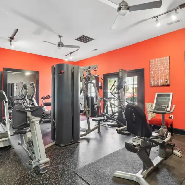 Interior of a modern gym with various fitness equipment on black flooring and bright orange walls.