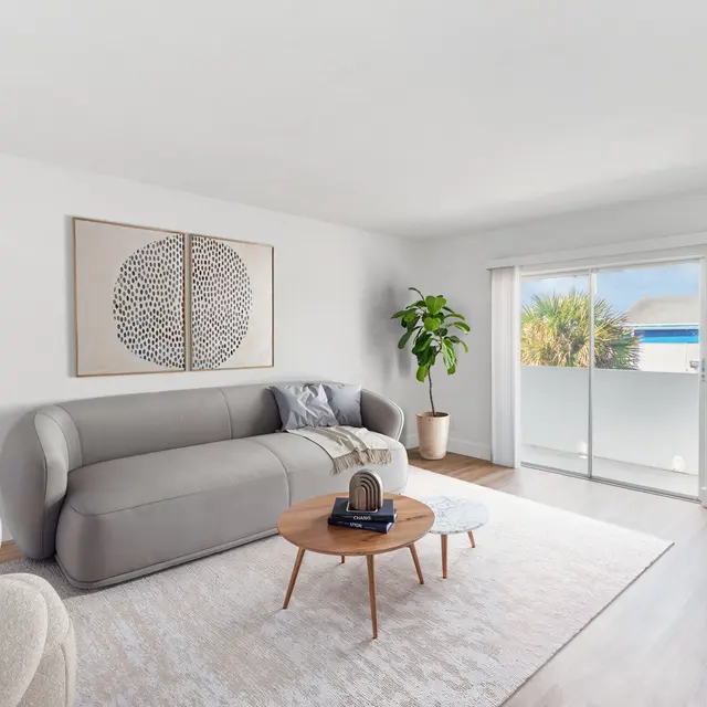 A bright and airy modern living room with a large couch, round coffee table, and greenery.
