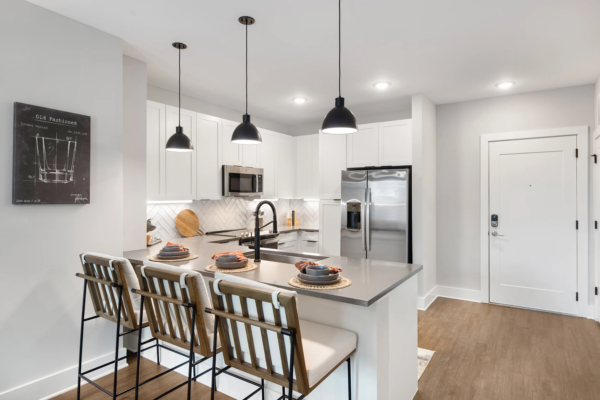 Modern Kitchen Interior A modern kitchen featuring white cabinetry, stainless steel appliances, and a large island with bar stools. There are pendant lights hanging above the island, and a decorative blackboard on the wall.