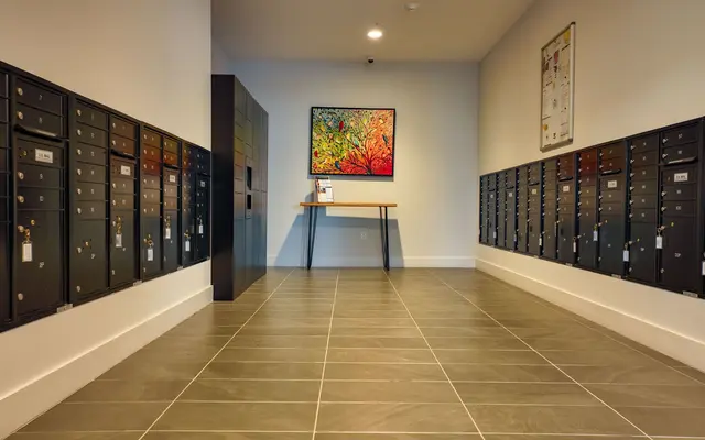 Interior view of a modern mail room with black mailboxes lined up against the walls and a colorful painting on the wall.