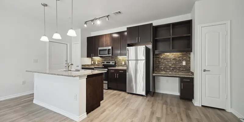 A modern kitchen featuring dark cabinetry, stainless steel appliances, and a light countertop with an island. The space has warm wooden flooring and stylish pendant lighting.