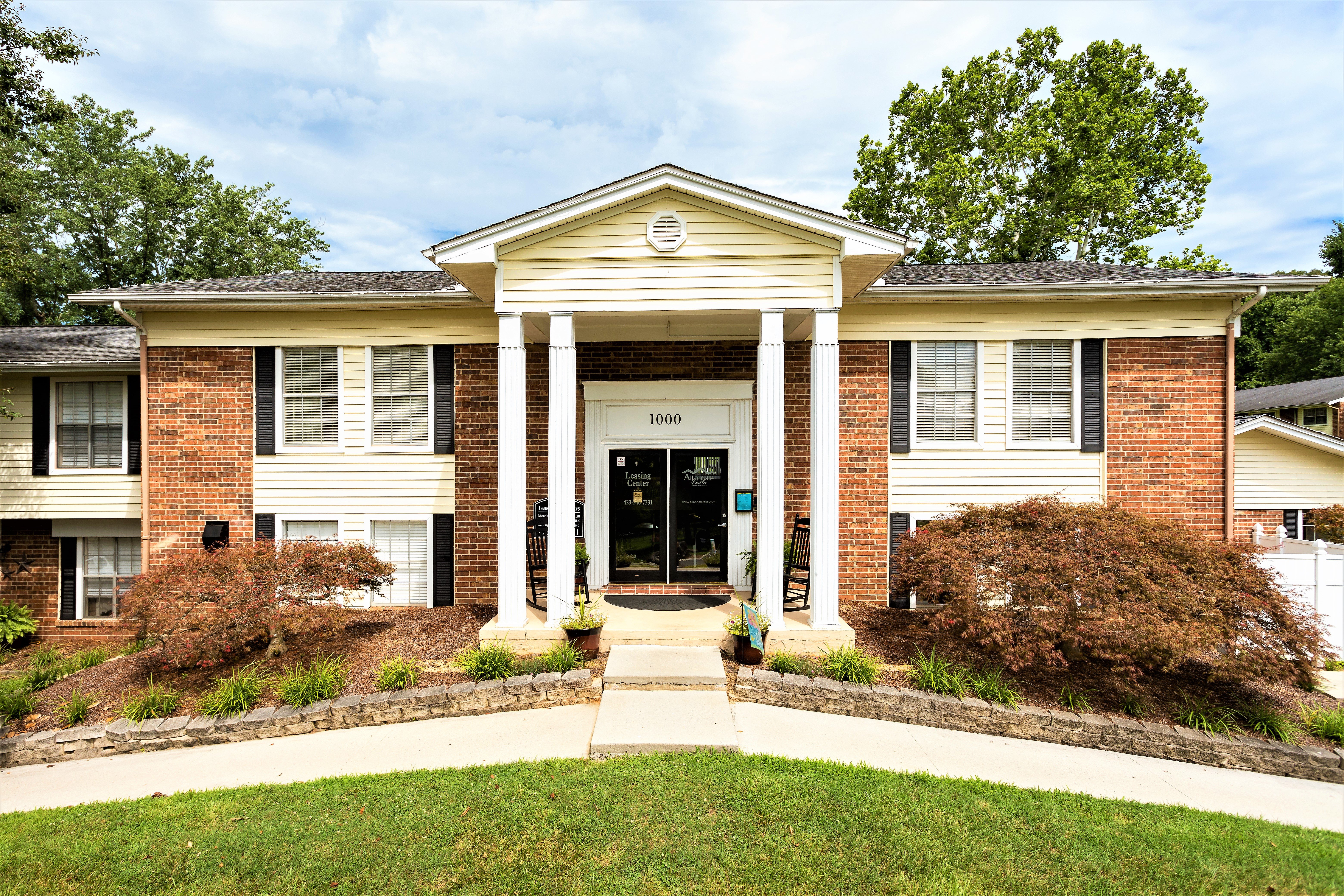 Front view of a two-story apartment building with brick and siding, featuring white columns and a landscaped entrance.