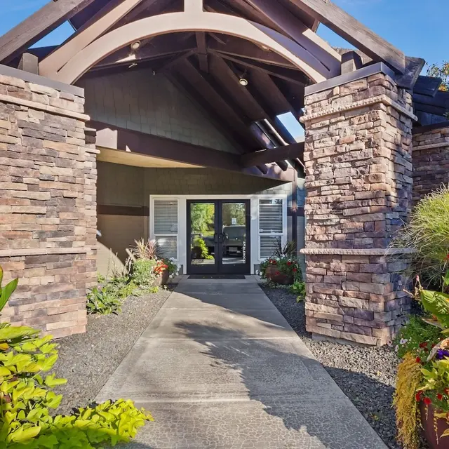 Monterra Townhomes - Welcoming Building Entrance Entrance of a building with a rustic stone facade and wooden beams, surrounded by colorful flowers and greenery.