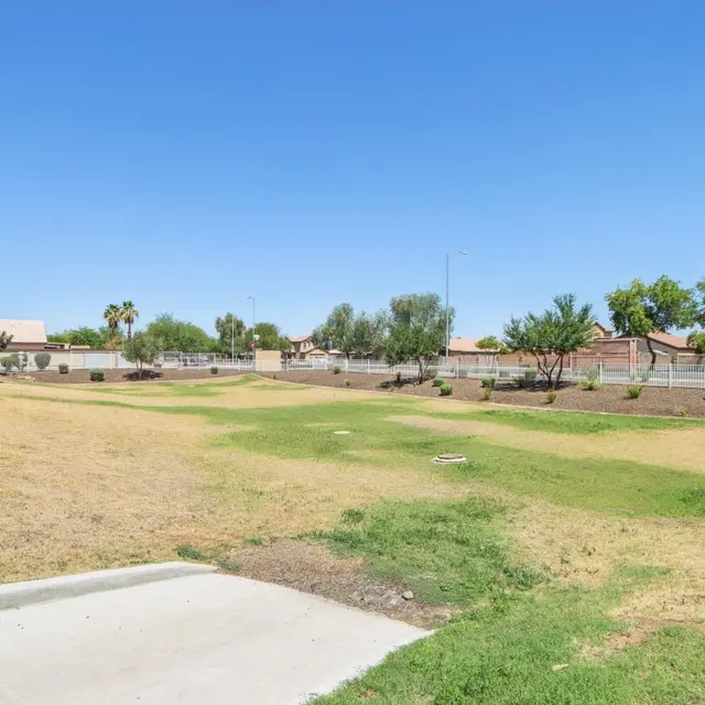 A wide view of a grassy park area with sparse trees and landscaping under a clear blue sky.