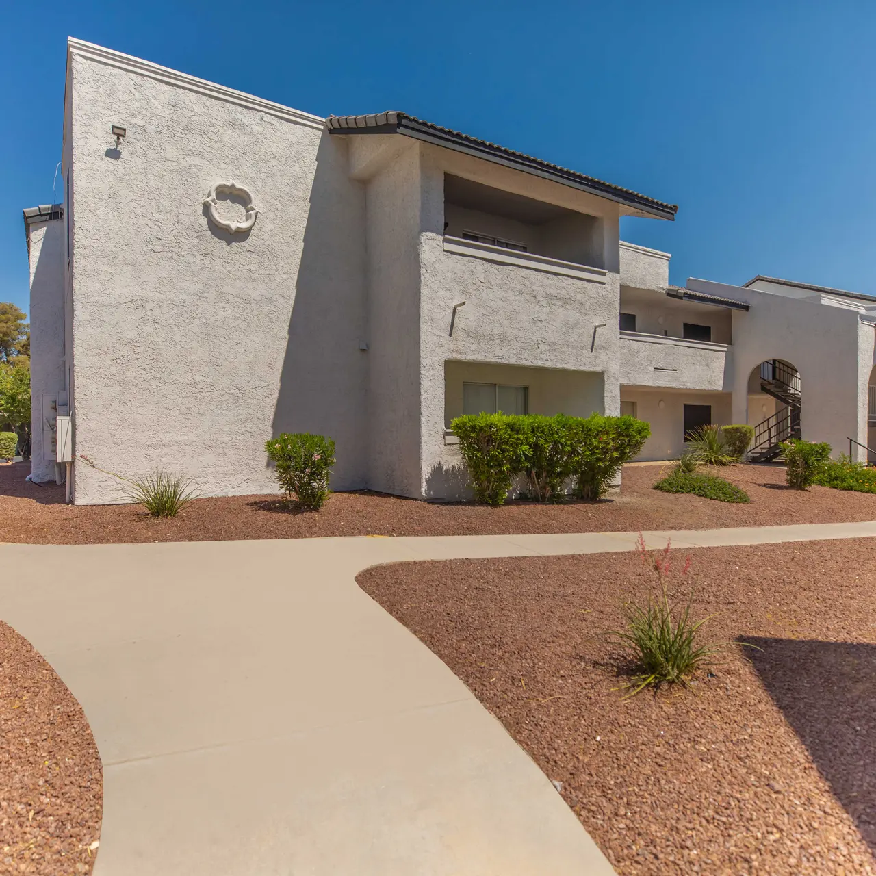 Exterior view of a multi-unit apartment complex with light-colored walls and greenery.