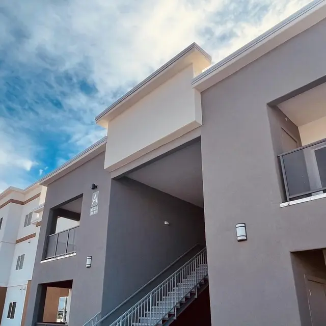 Exterior view of a modern apartment complex with a staircase and balconies, under a blue sky with clouds.