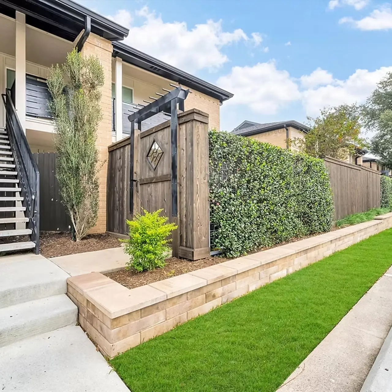 Exterior view of an apartment building with stairs, decorative fence, and landscaped pathway.