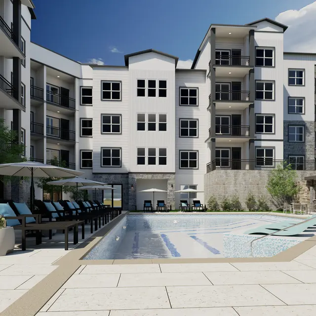 A modern apartment complex with a swimming pool, lounge chairs, and umbrellas. The building features multiple levels with balconies and large windows.