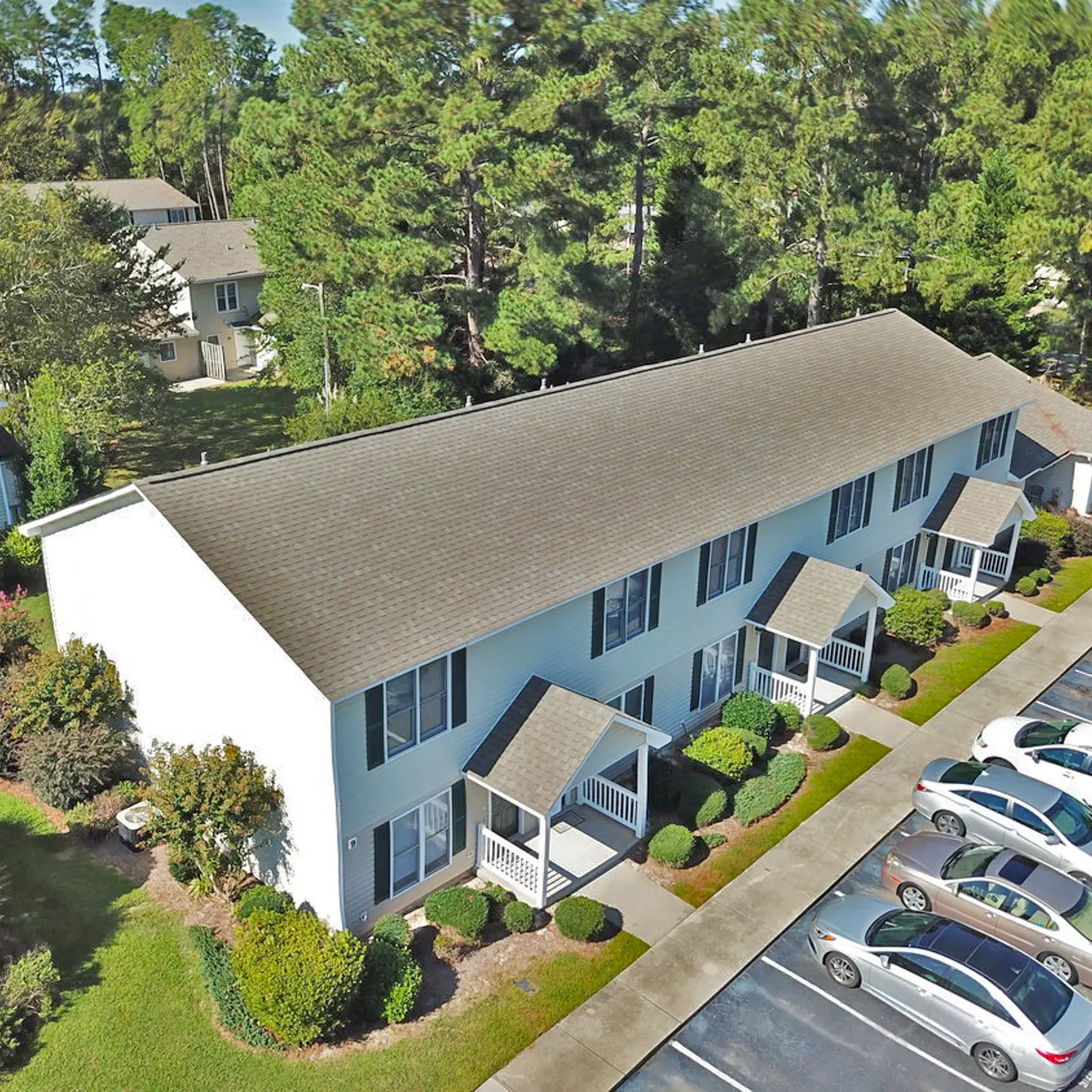 Aerial view of a residential apartment complex surrounded by trees and greenery with parking spaces in front.