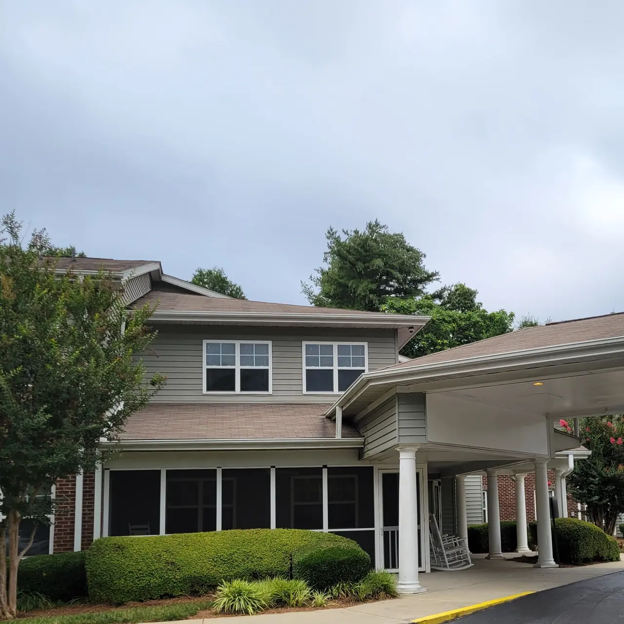 An exterior view of a residential building featuring a covered entrance, green bushes, and two-story architecture under a cloudy sky.