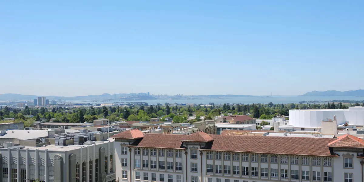 A wide-angle view of a scenic bay area with buildings and greenery in the foreground, featuring a blue sky and water in the background.