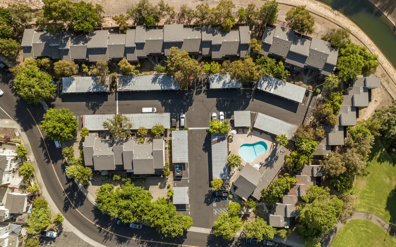 Aerial view of a residential apartment complex featuring multiple buildings arranged around a central pool area surrounded by greenery.