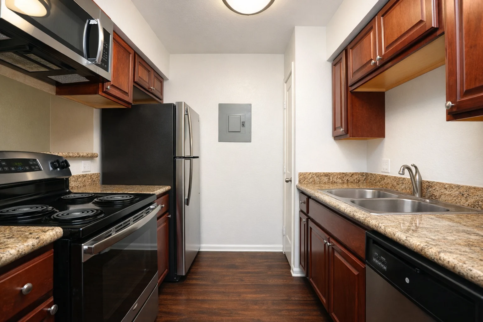 A modern kitchen featuring wooden cabinets, granite countertops, and stainless steel appliances including a refrigerator, oven, and microwave.