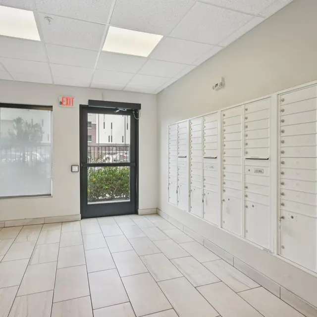 Mailroom Interior Interior view of a mailroom with white mailboxes lined on one wall and a door leading outside on the opposite side. There's a wire rack for magazines beside the door.