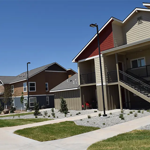 Exterior view of a modern apartment complex featuring two buildings with contrasting colors, a pathway, and landscaping including gravel and small plants.