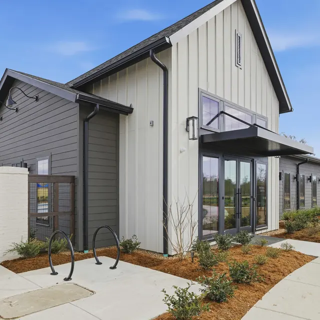 Modern Building Exterior A modern building with a combination of dark and light siding, featuring large glass windows, a covered entrance, and landscaped surroundings.