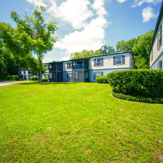 A well-maintained apartment complex with green lawns and trees under a clear blue sky.